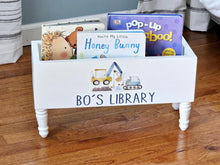 Load image into Gallery viewer, A white wooden children's bookshelf with turned legs and the words 'BO'S LIBRARY' printed on the front, holding several children's books on a hardwood floor.