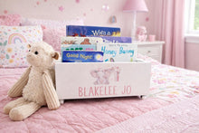 Load image into Gallery viewer, A personalized white wooden book bin with pink text reading 'BLAKELEE JO' and pink elephant illustrations, filled with children's books, styled on a pink quilted bed next to a plush teddy bear.