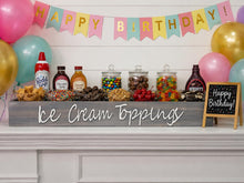 Load image into Gallery viewer, A styled birthday dessert bar setup with a large wooden sign reading 'Ice Cream Toppings' on a white mantel. The display includes jars of candy and nuts, bottles of syrup and whipped cream, and a small chalkboard sign that says 'Happy Birthday!'.