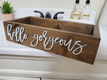 Load image into Gallery viewer, A rustic wooden decorative box with the phrase 'hello gorgeous' in white script, displayed on a bathroom counter with soap and lotion bottles in the background.
