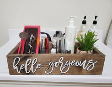 Load image into Gallery viewer, A rectangular wooden cosmetic organizer tray with the words 'hello gorgeous' in white script, filled with skincare and makeup items, a small succulent, and two pump bottles on a white surface against a light wall.
