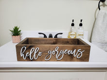 Load image into Gallery viewer, A rectangular rustic wooden vanity tray with the words 'hello gorgeous' in white script, displayed on a white bathroom counter with soap dispensers and a small plant.
