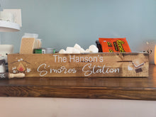 Load image into Gallery viewer, A rustic wooden sign reading 'The Hanson's S'mores Station' sits on a wooden shelf, styled with marshmallows, a bag of Reese's, and other s'mores-themed props against a blue wall.

