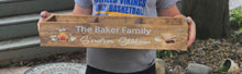 Load image into Gallery viewer, A person holding a wooden decorative tray outdoors. The tray is light brown wood with white printed text reading 'The Baker Family' and 'S'mores Station' along with small illustrations of a fire pit, marshmallow, and chocolate bar.
