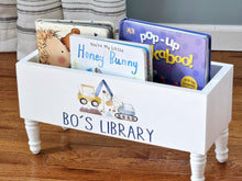 Load image into Gallery viewer, A white wooden children's book box with legs, printed with the words 'BO'S LIBRARY' and construction vehicle illustrations, filled with baby board books on a wooden floor.
