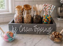 Load image into Gallery viewer, A wooden sign reading 'Ice Cream Toppings' in a kitchen setting, holding glass jars filled with sprinkles, cereal pieces, chocolate chips, and colorful candies, with bowls of ice cream topped in front.
